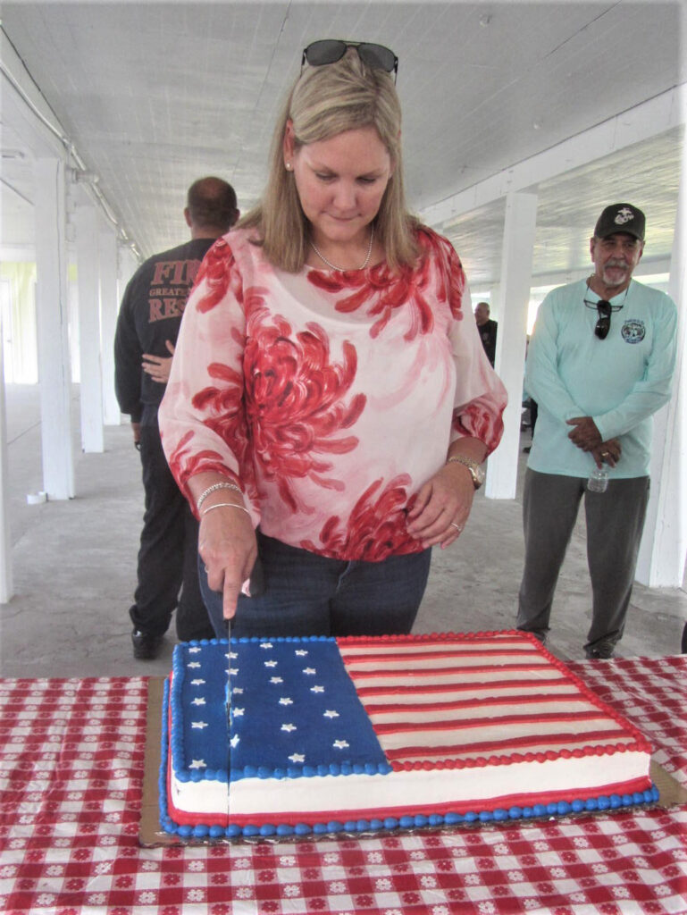 A woman cuts a sheet cake, which has an American Flag design.